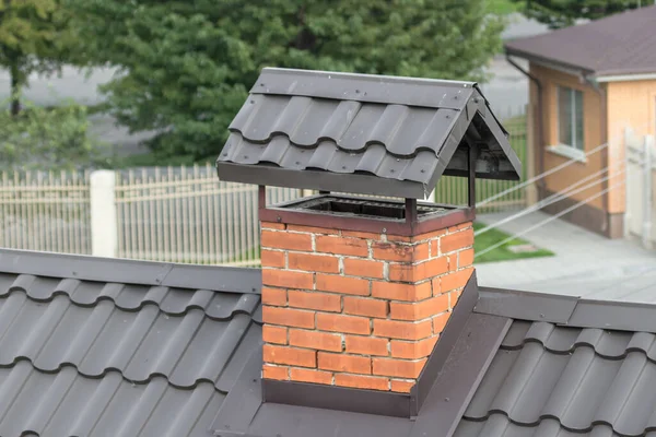 Brick chimney on the roof. Private residential building. Slate covering. Fireplace in the house. Alternative heating in the house. Roof hole.