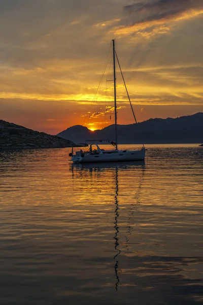 Lonely small yacht near harbor Panormitis and orange clouds at sunset on Symi Island