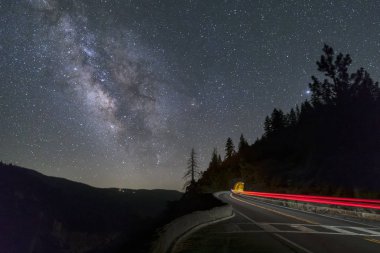 Samanyolu ile gece gökyüzünün altında Kaliforniya'nın Yosemite Milli Parkı'büyük meşe düz yolda otomobil farları çizgi sahne ve bir tünel içine parlak.