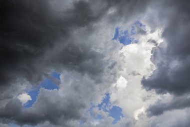 Mavi gökyüzü ve parlak beyaz bulutlar daha koyu, fırtınalı bulutlar ötesinde aşağıda görülmektedir.