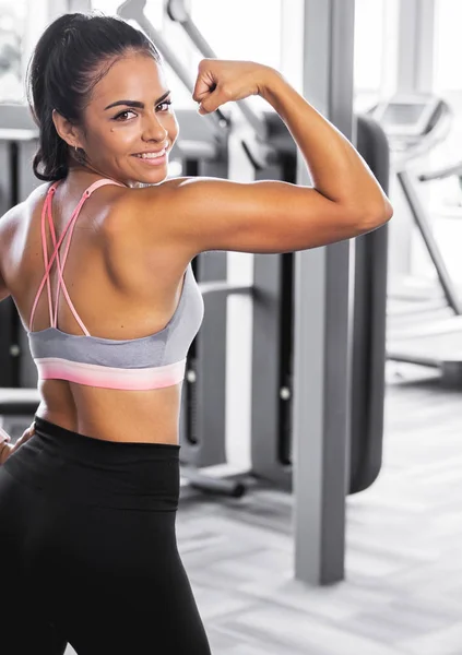 Beautiful slim smiling woman in gym posing flexing her muscles