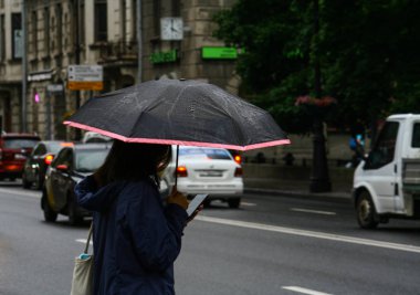 Asyalı kız büyük bir şehir sonbahar bulutlu gün sokakta yağmurda bir şemsiye altında dururken bir telefon kullanır