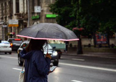 Asyalı kız büyük bir şehir sonbahar bulutlu gün sokakta yağmurda bir şemsiye altında dururken bir telefon kullanır