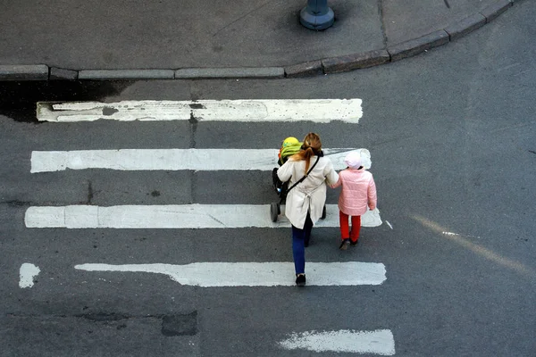Μια γυναίκα με καροτσάκι και η κόρη της να διασχίζουν το δρόμο μια ανοιξιάτικη μέρα. Πίσω όψη από το παράθυρο — Φωτογραφία Αρχείου