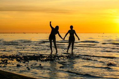 Denizde gün batımında iki kız siluetleri