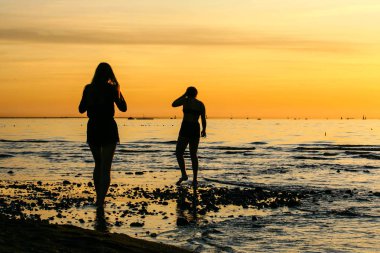 Denizde gün batımında iki kız siluetleri