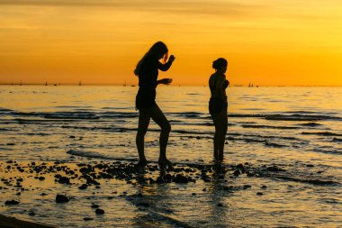 Denizde gün batımında iki kız siluetleri