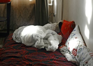 Siyah-kırmızı süslenmiş çarşaf, beyaz buruşuk battaniye ve bir kırmızı ve iki beyaz işlemeli yastık ile unmade yatak