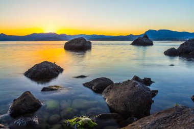 sessiz deniz gün batımında suda taşlarla defne