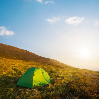 Günbatımında bir tepenin yamacında yeşil turistik çadır