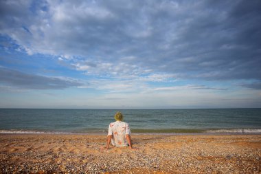Bir adam deniz kıyısında oturur dramatik bulutlu gökyüzünün altında, yaz deniz macerası sahnesinde
