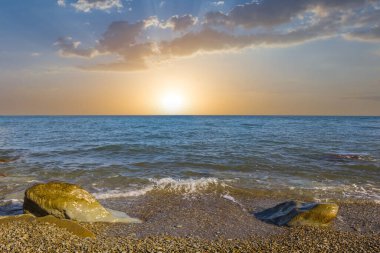 Güneş batarken taşlı deniz kıyısında, yaz akşamı sahnesinde