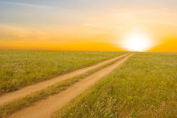 日落时的草原间的地面道路 — 图库照片