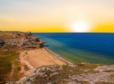 Güneş batarken taşlı sahilleri olan zümrüt deniz koyunda