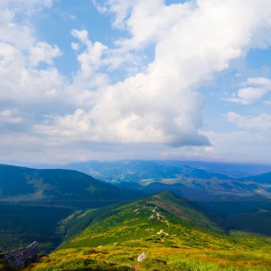 Mavi bulutlu gökyüzünün altındaki yeşil dağ sırtı