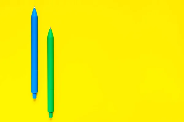 Blue and green color pens isolated on yellow background. Minimalist flat lay. Copyspace. Concept work and education. Office school supplies. Closeup view.