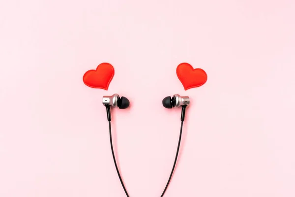 Pembe pastel arka planda akıllı telefon için siyah kulaklıklı kırmızı kalpler. Romantik ve aşk kavramı. Güzel hediye kartpostalı. Minimalist düzlük. Yazmak için boş bir yer. Uzayı kopyala Üst görünüm. 