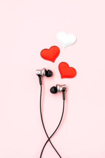 White and red hearts with black music earphones for smartphone on pink pastel background. Romantic and love concept. Listen your heart concept. Beautiful gift postcard. Vertical view.