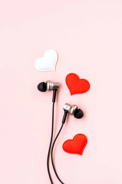 Red and white hearts with black music earphones for smartphone on pink pastel background. Romantic and love concept. Beautiful gift postcard. Minimalist flat lay. Vertical view.