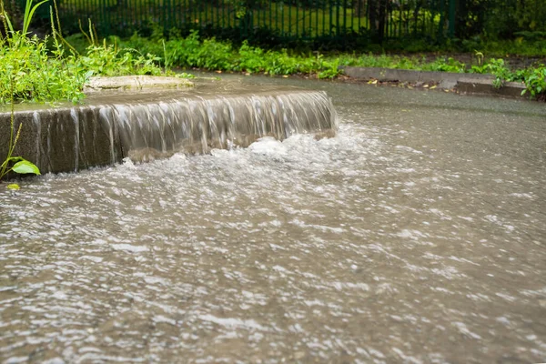 Su akıntısı yaya bölgesine doğru akmaktadır. Yağmurlu sonbahar havası. Şiddetli yağmur. Yağmurda sokak sahneleri.