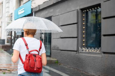 Şeffaf şemsiyeli bir kadın yağmurlu havada şehirde dolaşır. Yağmur damlalı şemsiye. Kötü yağmurlu havada şehir manzaraları.