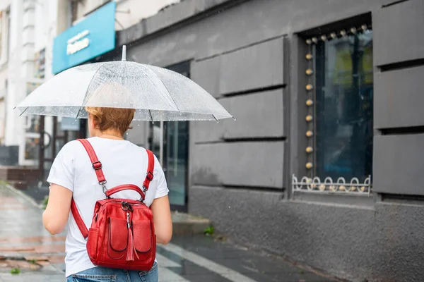 Şeffaf şemsiyeli bir kadın yağmurlu havada şehirde dolaşır. Yağmur damlalı şemsiye. Kötü yağmurlu havada şehir manzaraları.