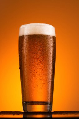 Turuncu arka planda köpüklü bir bardak bira.