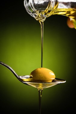 Zeytinyağı ve kaşık üzerinde yeşil zeytin