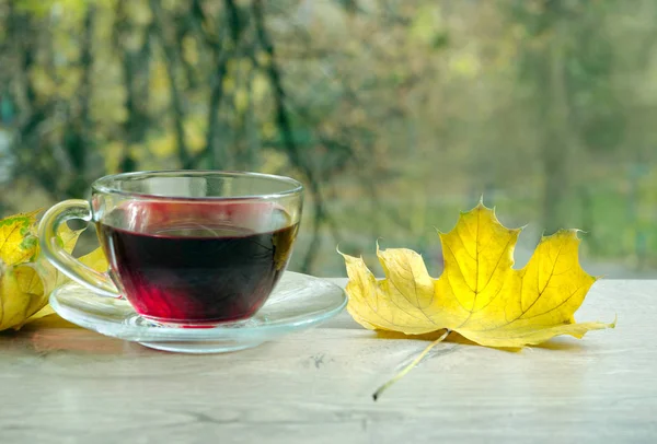 Cup of hibiscus tea and yellow leaves on a wooden table. Cup with hot hibiscus tea on wood table over autumn background.