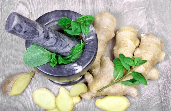 Stone pestle and mortar with mint leaves and ginger on a wooden table. top view. cold and flu remedy.