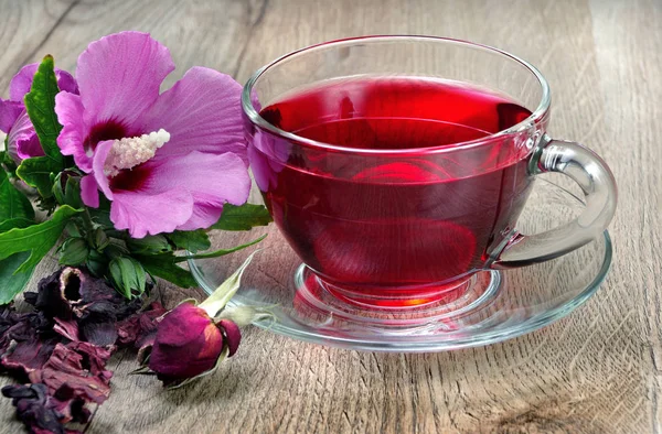Hibiscus tea in a glass cup on a wooden table among the rose petals and dry tea. Hibiscus flower. Vitamin tea for cold and flu