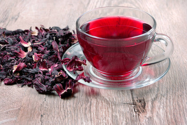 Hibiscus tea in a glass cup on a wooden table among the rose petals and dry tea. top view. Vitamin tea for cold and flu.