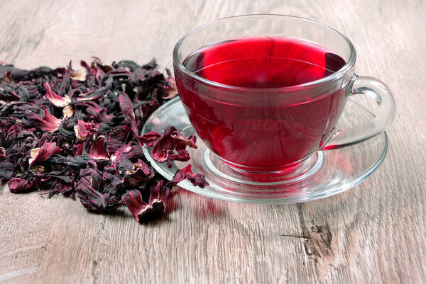 Hibiscus tea in a glass cup on a wooden table among the rose petals and dry tea. top view. Vitamin tea for cold and flu.