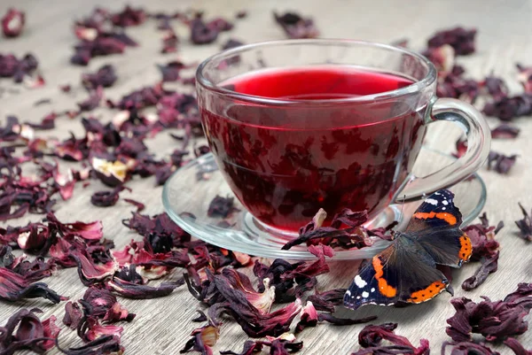 Hibiscus tea in a glass cup on a wooden table among the rose petals and butterfly admiral. Vitamin tea for cold and flu.