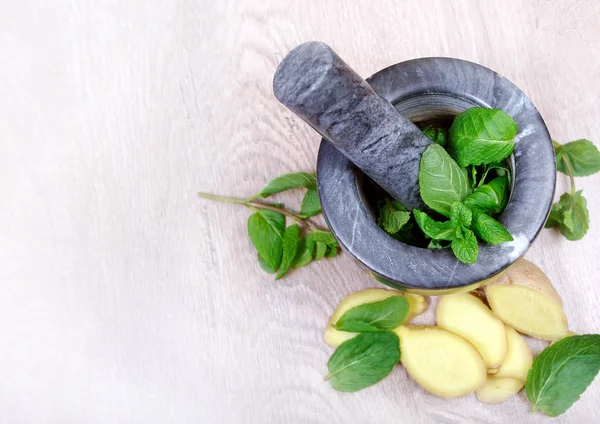 Stone pestle and mortar with mint leaves and ginger on a wooden table. top view. cold and flu remedy.