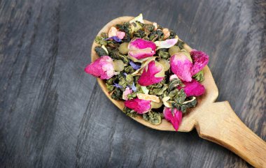 yeşil çay ile koyu ahşap bir masa üzerinde bir tahta kaşık çiçeklenir. yeşil çay çiçek ve kuru meyve parçaları ile. çay karışımı. Üstten Görünüm.
