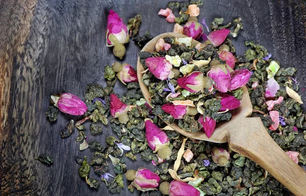花放在一个木勺在一个黑暗的木桌上 绿茶与花和干果片 混合茶 顶视图 — 图库照片