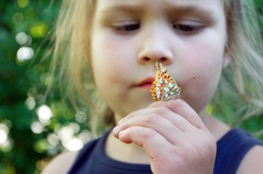 Kelebek bir çocuğun elinde oturuyor. Kelebekli çocuk. Küçük bir kızın elinde İspanya'nın Kelebek Kraliçesi fritillary. Seçici odaklama.