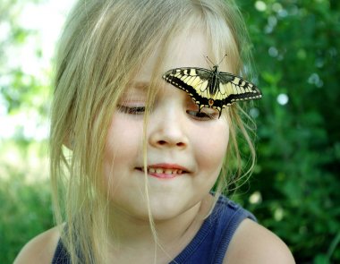 Kelebek bir çocuğun üzerinde oturuyor. Kelebekli çocuk. Kelebek machaon küçük bir kız üzerinde. Seçici odak. Kırlangıç kuyruğu kelebeği, Papilio maçaonu.