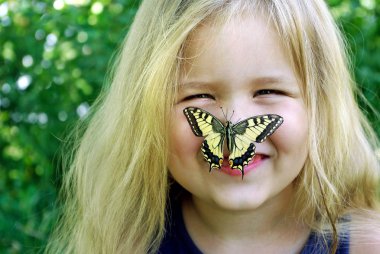 Kelebek bir çocuğun üzerinde oturuyor. Kelebekli çocuk. Kelebek machaon küçük bir kız üzerinde. Seçici odak. Kırlangıç kuyruğu kelebeği, Papilio maçaonu.