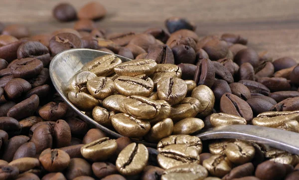 Gold coffee beans on a pile of coffee beans. The concept of luxury is extraordinary. Coffee beans in a spoon. Golden coffee beans texture background