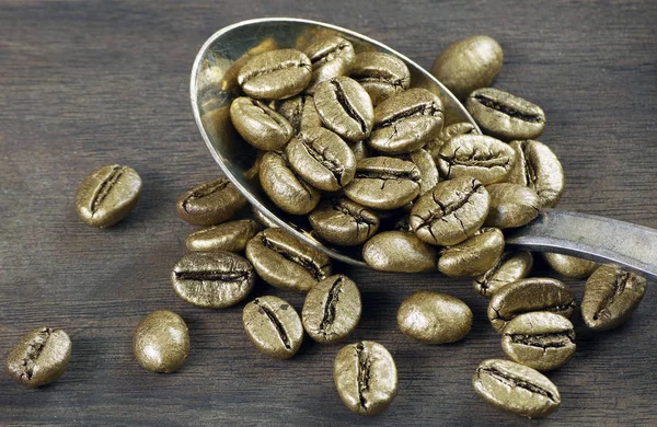 Gold coffee beans on a pile of coffee beans. The concept of luxury is extraordinary. Coffee beans in a spoon. Golden coffee beans texture background