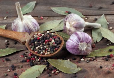 Mutfak için geleneksel baharatlar. Koyun yaprağı, kaşıkta çeşitli biberler ve ahşap bir masada sarımsak karışımı. Üst Manzara. Boşlukları kopyala