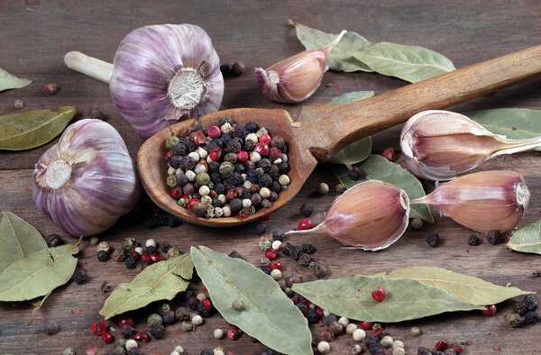 traditional spices for the kitchen. bay leaf, mixture of various peppers in a spoon and garlic on a wooden table.