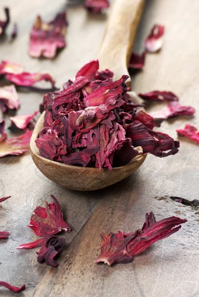 dry hibiscus in a wooden spoon. dried hibiscus petals on a wooden table. hibiscus tea.  vitamin tea for cold and flu.