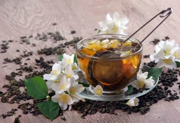 green tea with jasmine. dry green tea leaves with jasmine flowers and a cup of tea on a wooden table. close up