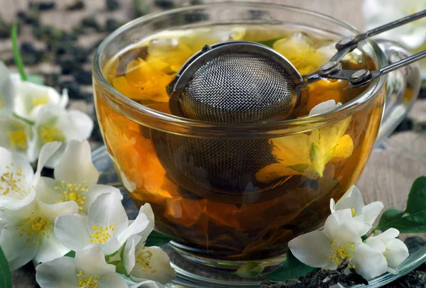 green tea with jasmine. dry green tea leaves with jasmine flowers and a cup of tea on a wooden table. close up