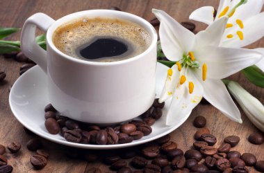 Beyaz bardakta kahve. Bir fincan kahve, kavrulmuş kahve çekirdekleri ve ahşap bir masada beyaz zambak çiçeği. Romantik kahve. Kapat.