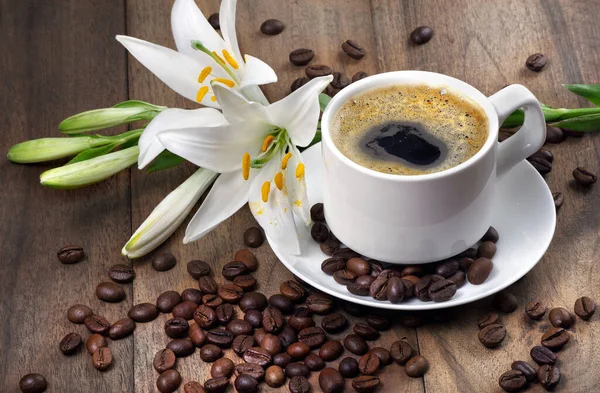 coffee in a white cup. cup of coffee, roasted coffee beans and white lily flower on a wooden table. romantic coffee. close up