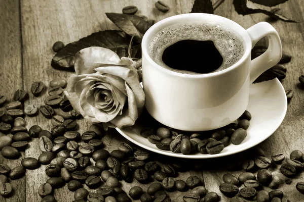 coffee in a white cup. cup of coffee, roasted coffee beans and tender rose on a wooden table. romantic coffee black and white